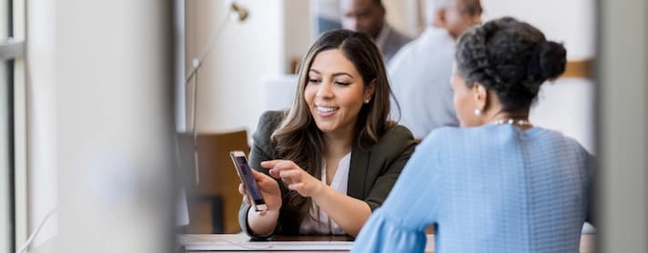 Professionista sorridente che mostra informazioni sullo smartphone a un’altra persona durante una consulenza.