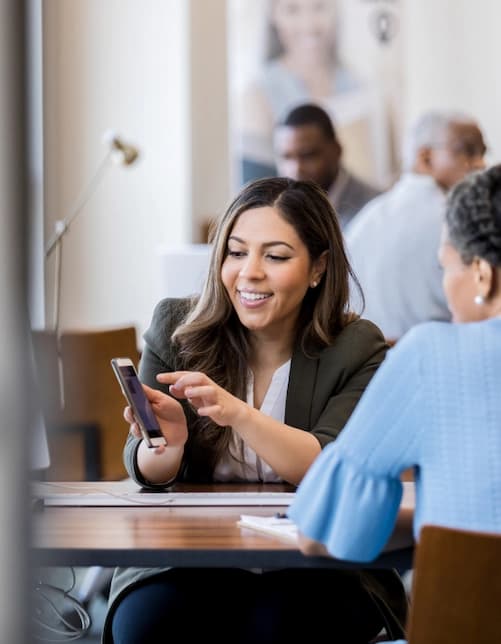 Professionista sorridente che mostra informazioni sullo smartphone a un’altra persona durante una consulenza.