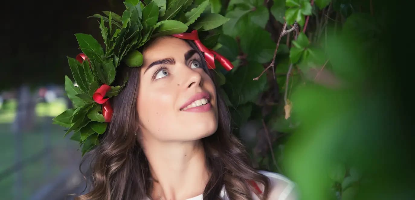 Giovane laureata con corona di alloro in testa, simbolo della laurea in Italia, sorridente e immersa nella natura.
