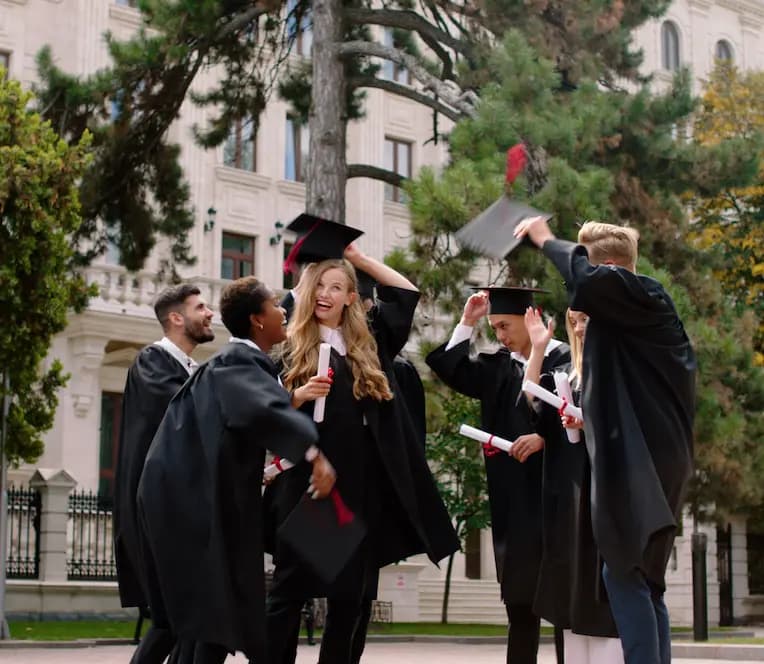  Gruppo di studenti in abiti da laurea che festeggiano all’aperto, lanciando i cappelli in aria e tenendo in mano i diplomi.