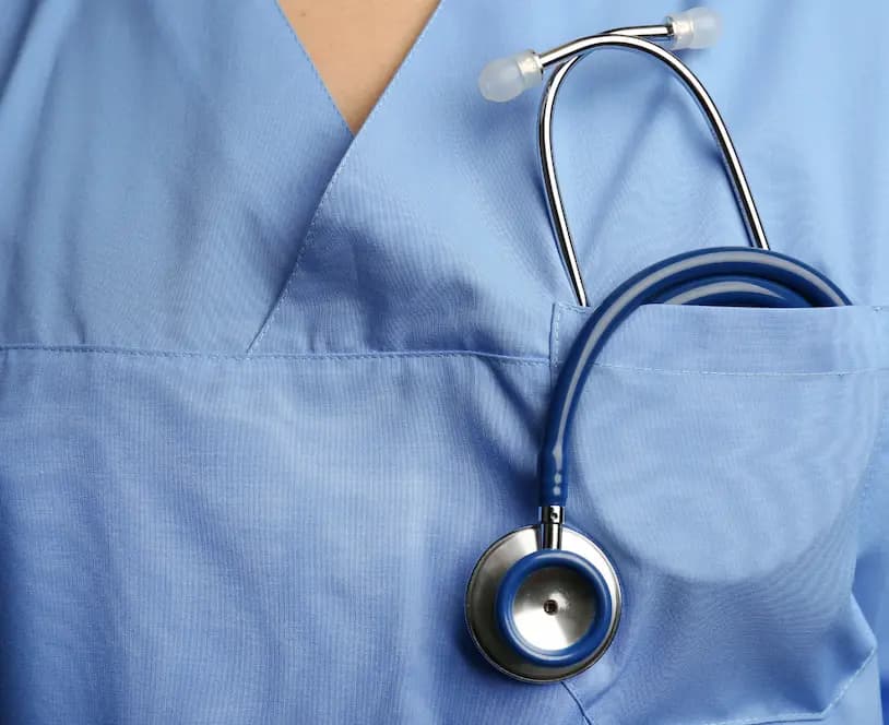 Primo piano di un camice medico azzurro con stetoscopio riposto nella tasca.